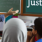 A teacher interacting with students in a classroom, discussing societal implications of justice
