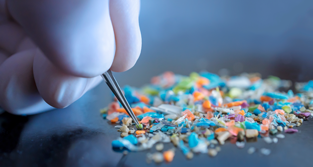 A gloved hand uses tweezers to examine colorful microplastics on a dark surface, highlighting environmental pollution and research efforts.